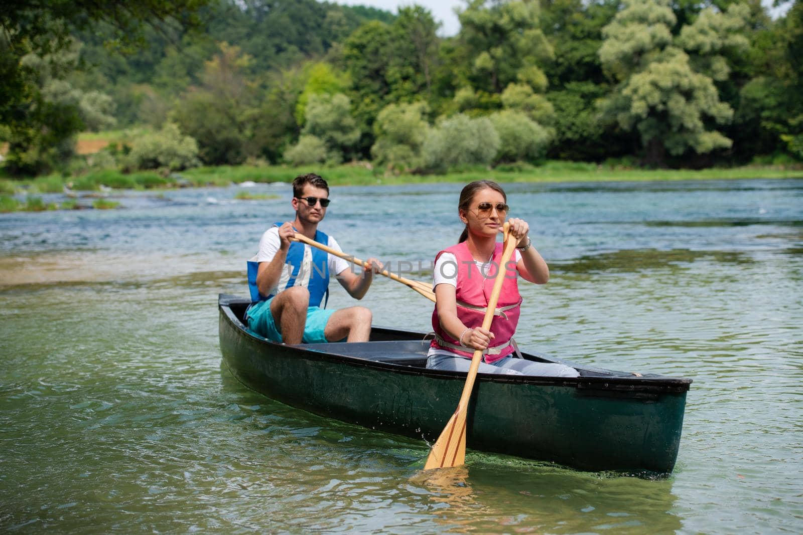 Couple adventurous explorer friends are canoeing in a wild river surrounded by the  beautiful nature