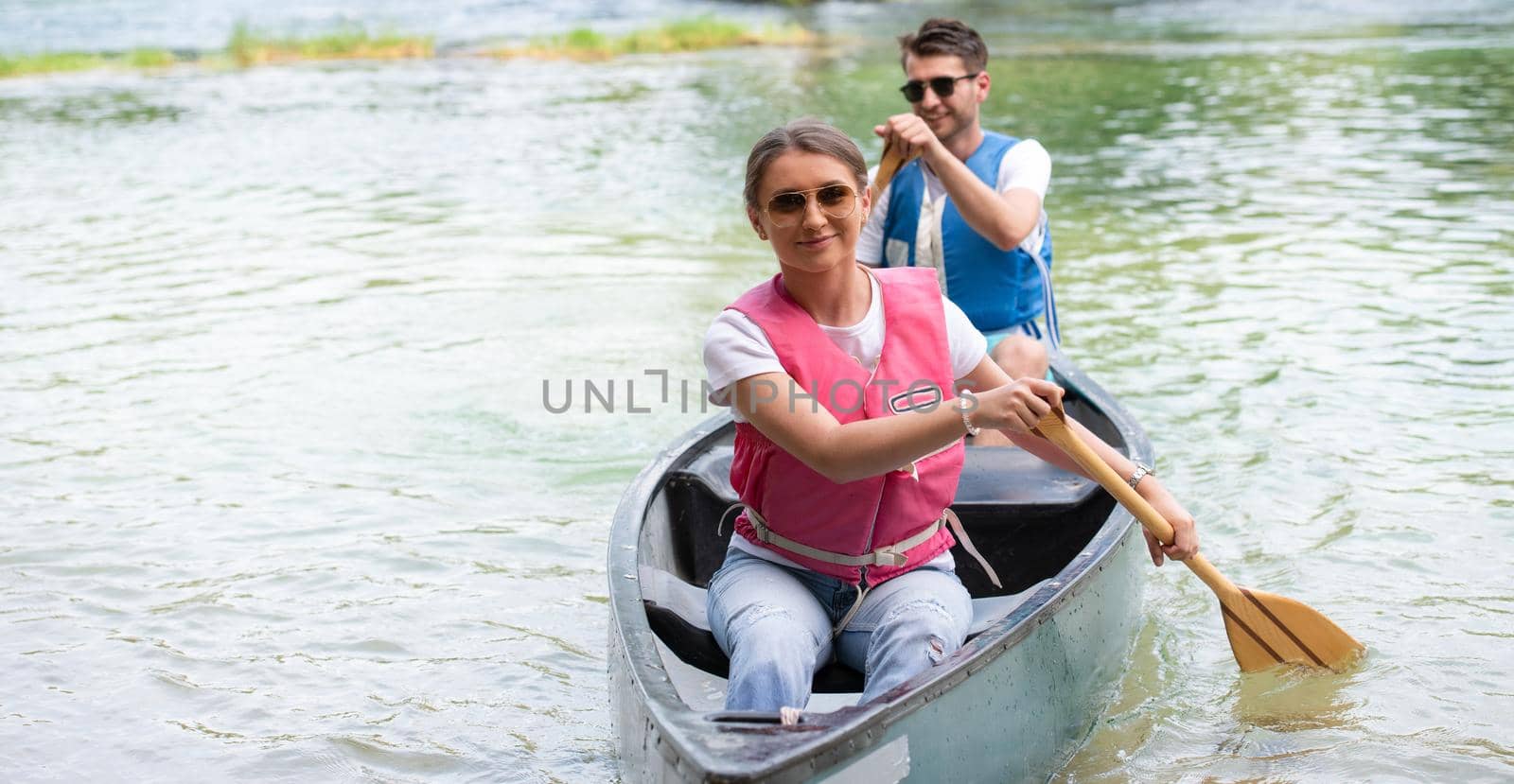 Couple friends are canoeing in a wild river surrounded by the  beautiful nature