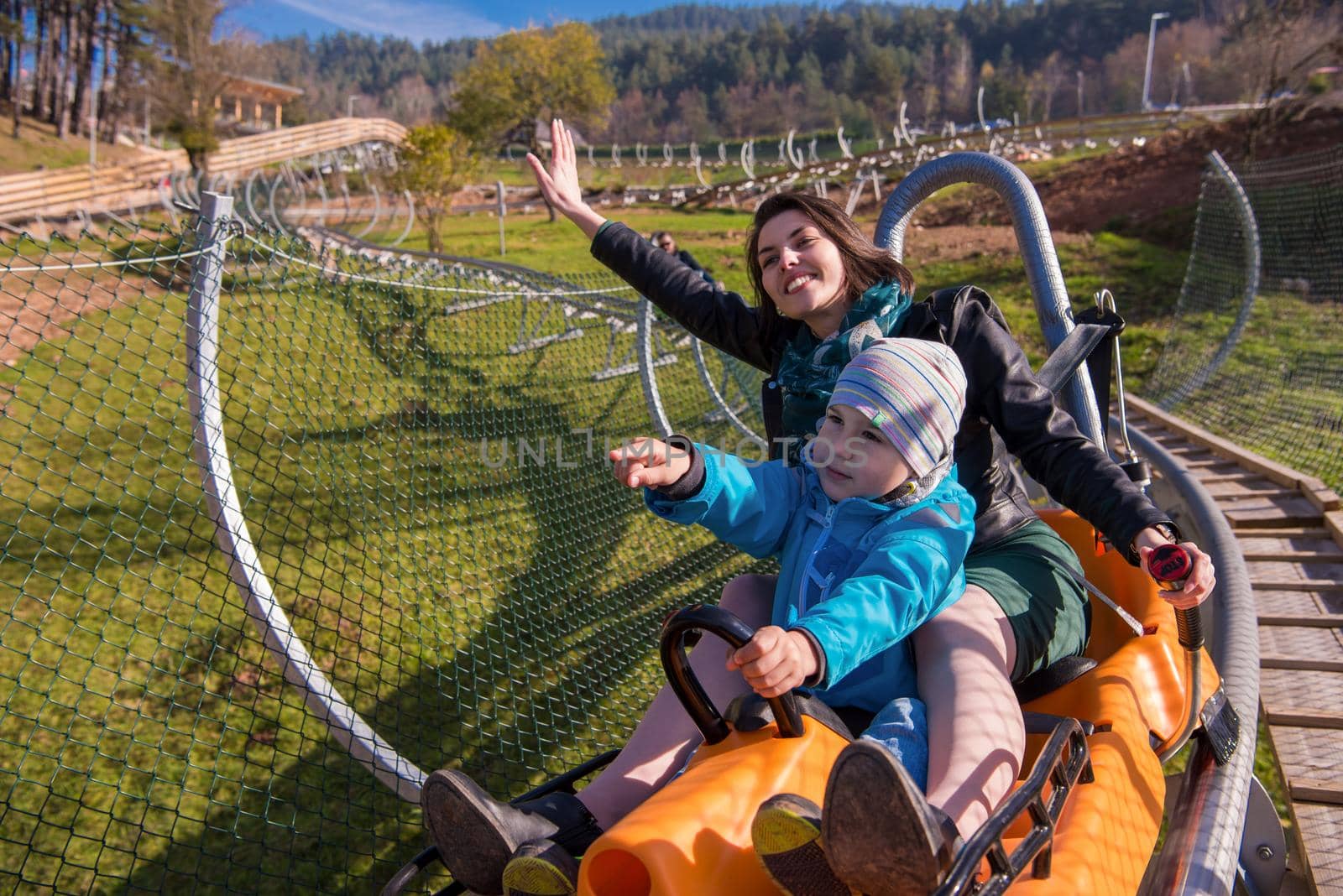 Excited young mother and son driving on alpine coaster while enjoying beautiful sunny day in the nature