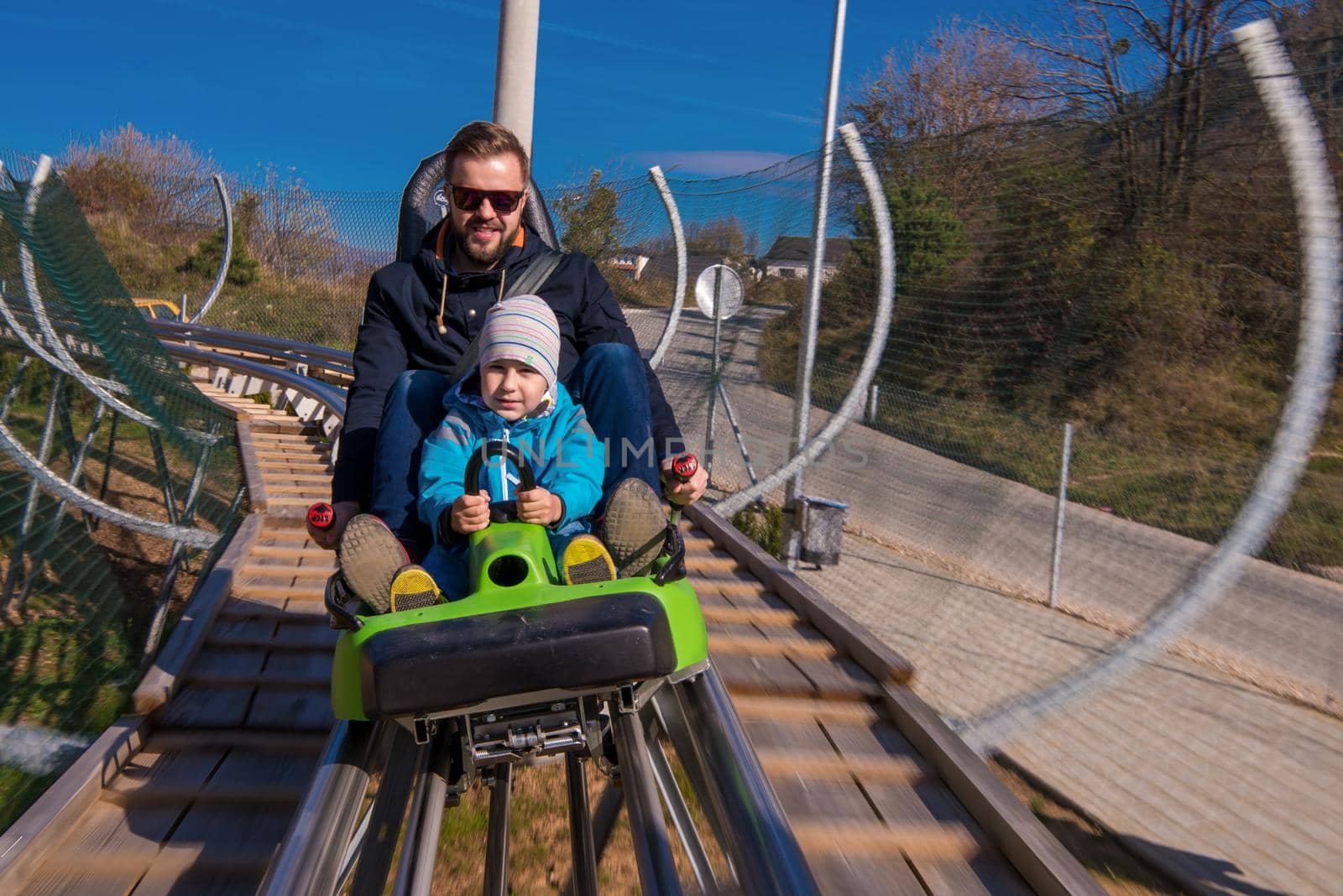 Excited young father and son driving on alpine coaster while enjoying beautiful sunny day in the nature