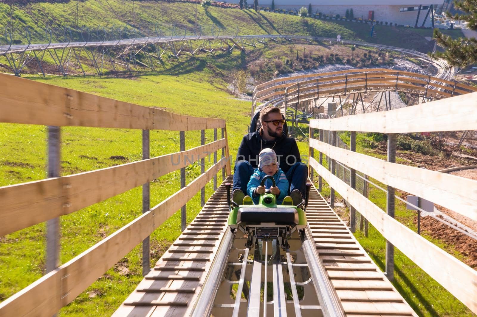 Excited young father and son driving on alpine coaster while enjoying beautiful sunny day in the nature