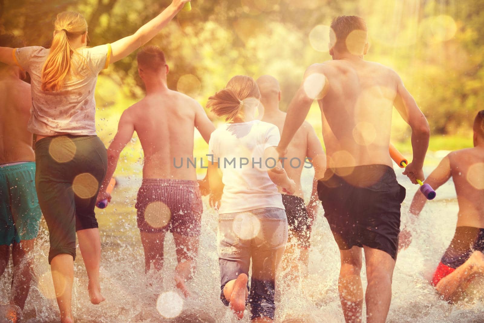 summer joy group of happy friends having  fun while running and splashing on river