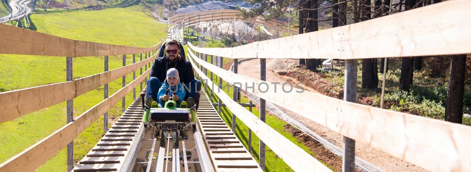 Excited young father and son driving on alpine coaster while enjoying beautiful sunny day in the nature