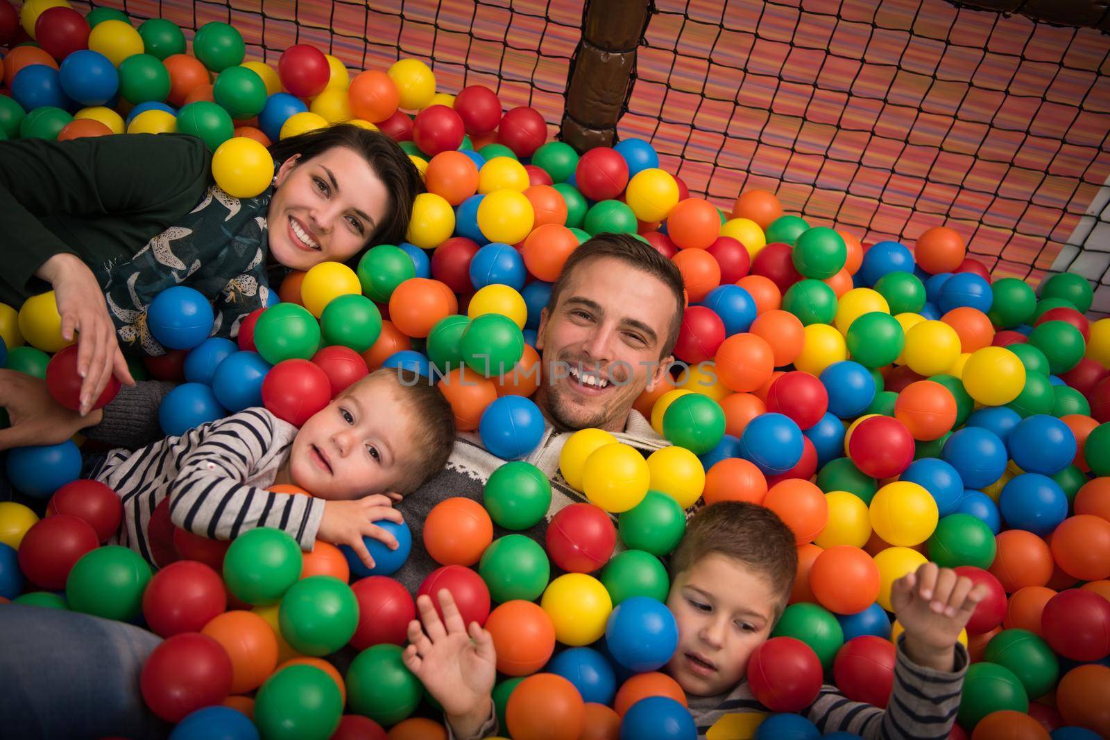 Happy young parents are playing with their kids at pool with colorful balls in a children's playroom