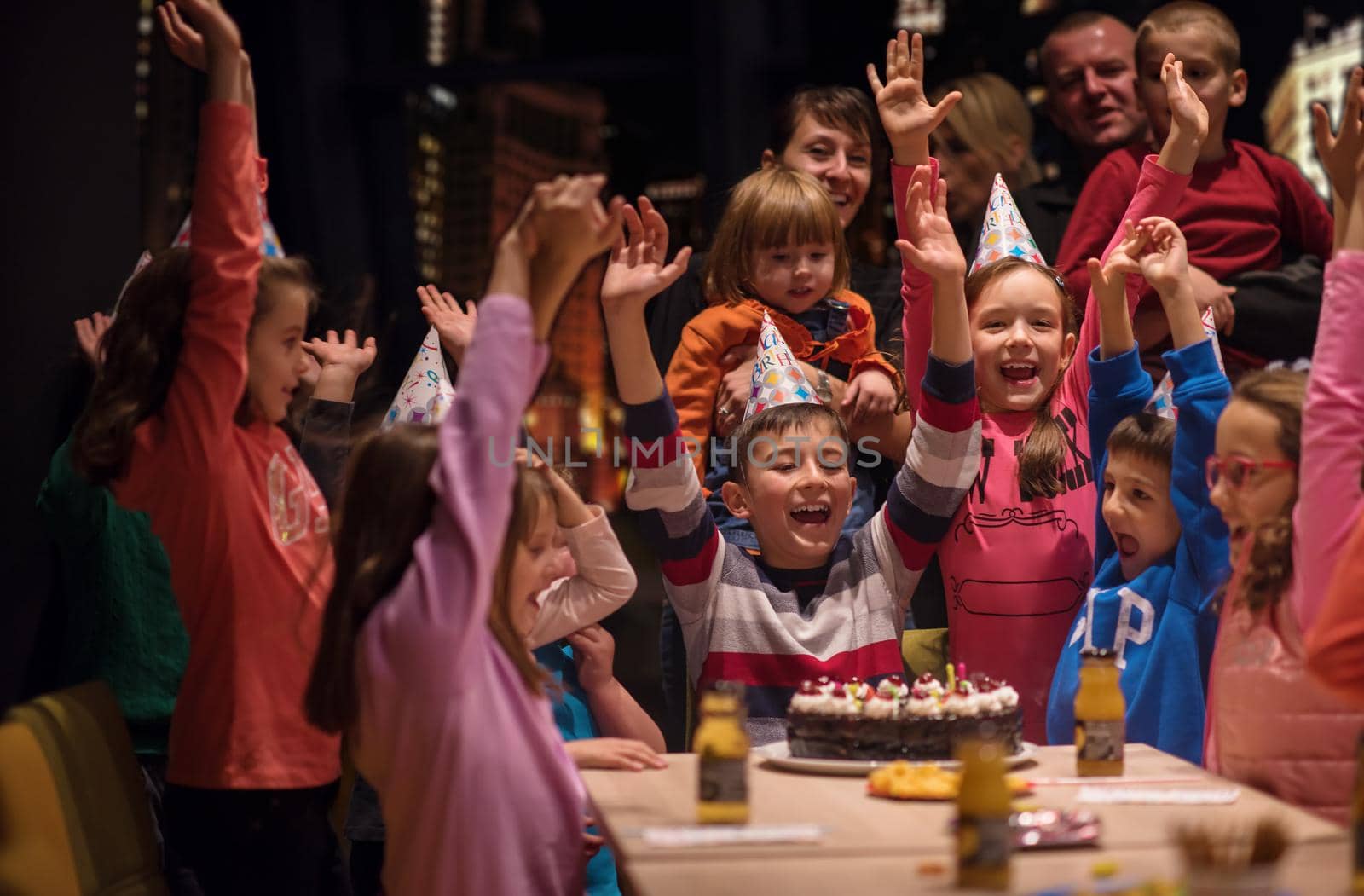 young happy boy and group of his friends having birthday party with a night city through the windows in the background