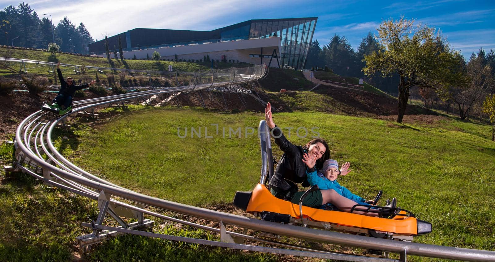 Excited young mother and son driving on alpine coaster while enjoying beautiful sunny day in the nature