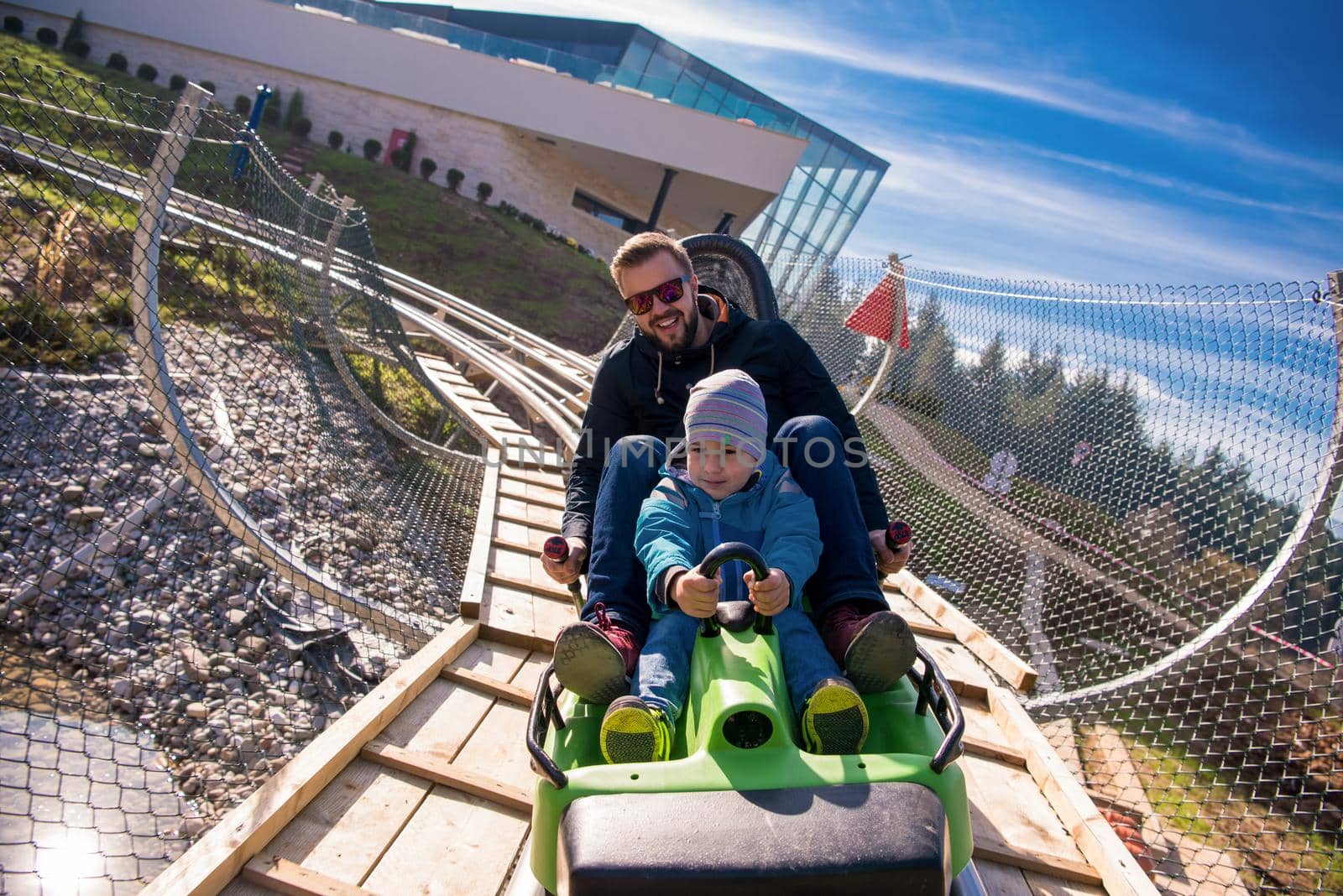 Excited young father and son driving on alpine coaster while enjoying beautiful sunny day in the nature