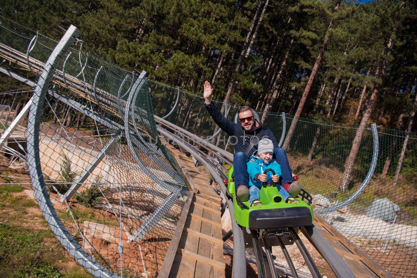 Excited young father and son driving on alpine coaster while enjoying beautiful sunny day in the nature