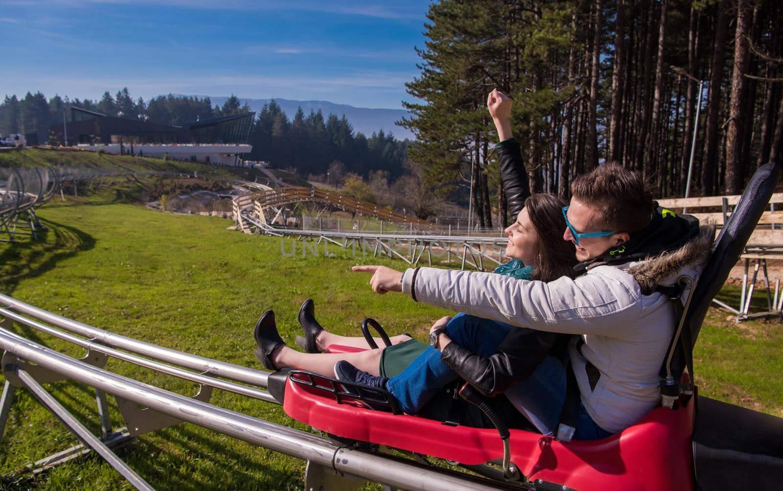 Excited young couple driving alpine coaster while enjoying beautiful sunny day in the nature