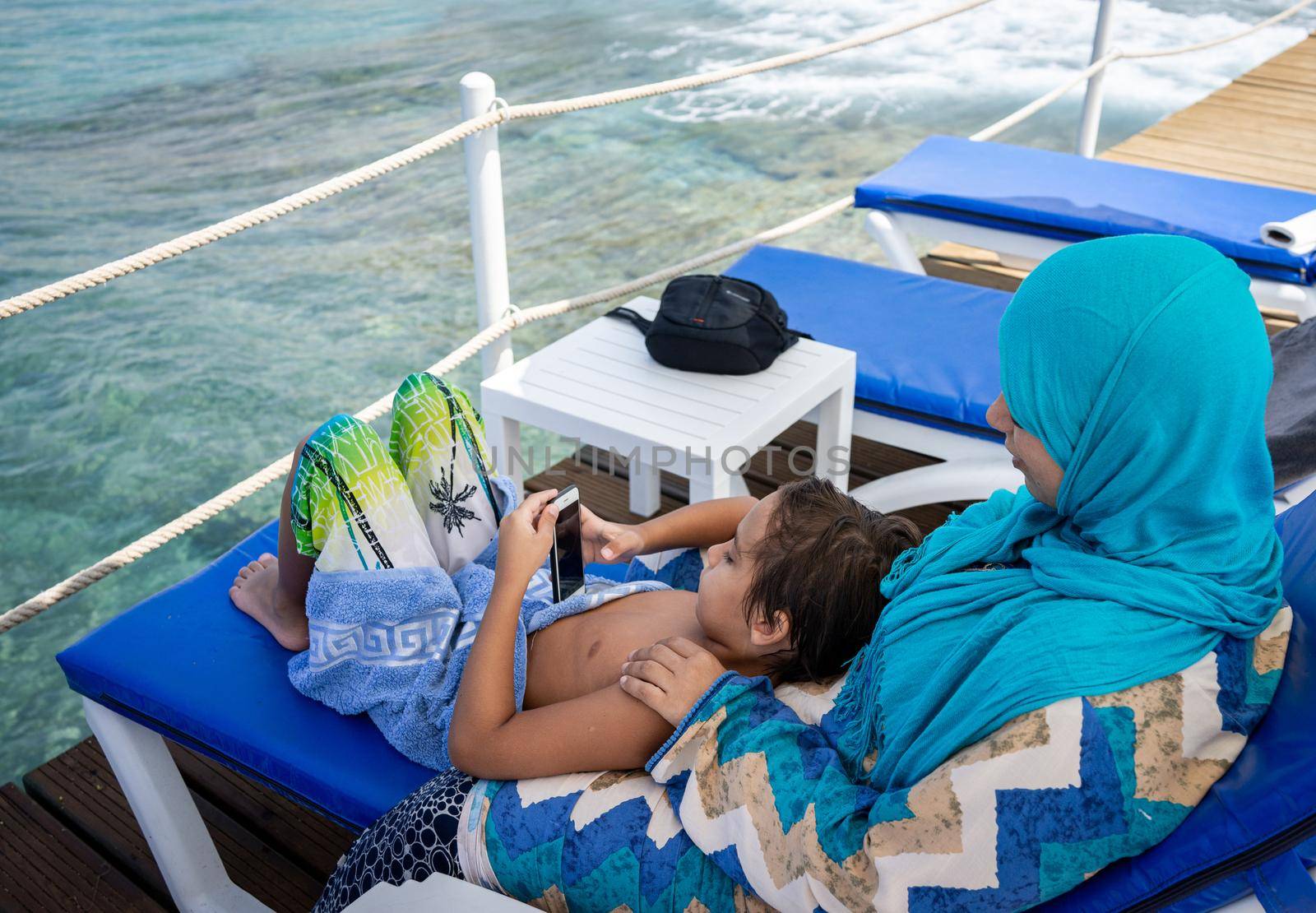 Arabic mother and son sitting and enjoying on beach pier by Zurijeta