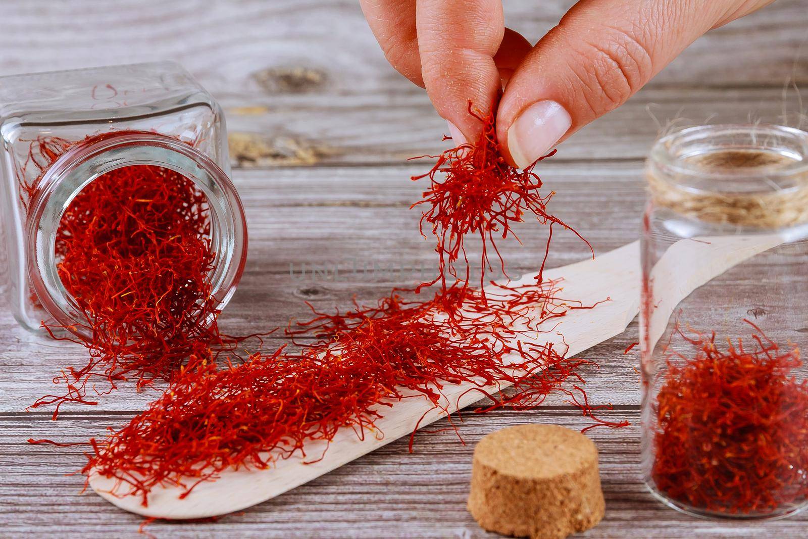 The girl puts the saffron in a glass container. Saffron spice in a glass bottle and on a wooden spoon on a wooden background.