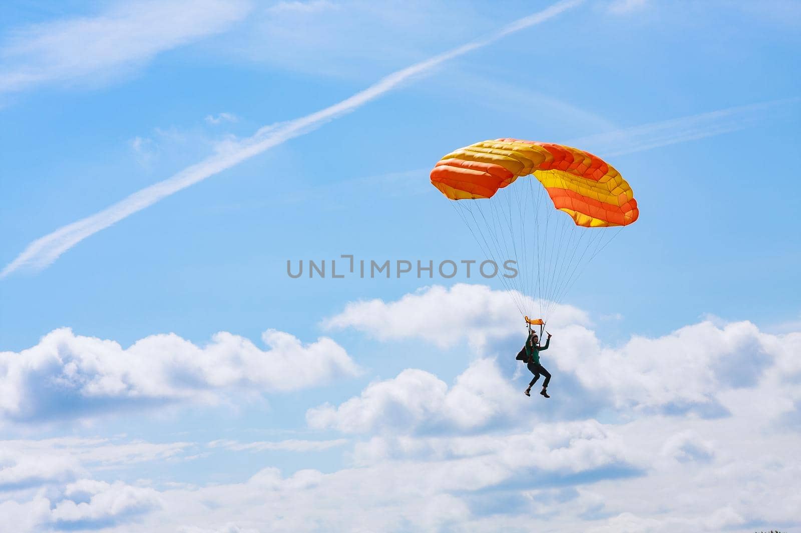 Skutech, Czech Republic, 6 August 2020: A parachutist with an orange parachute canopy against a background of blue sky and white clouds. Skydiving.