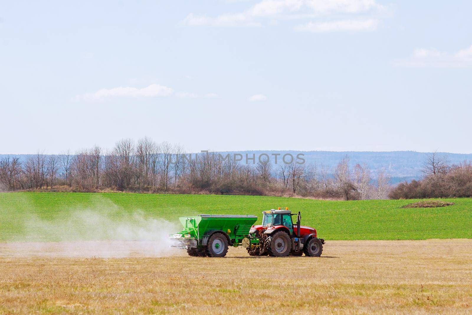 Agricultural work. Tractor spreading fertilizer on grass field.