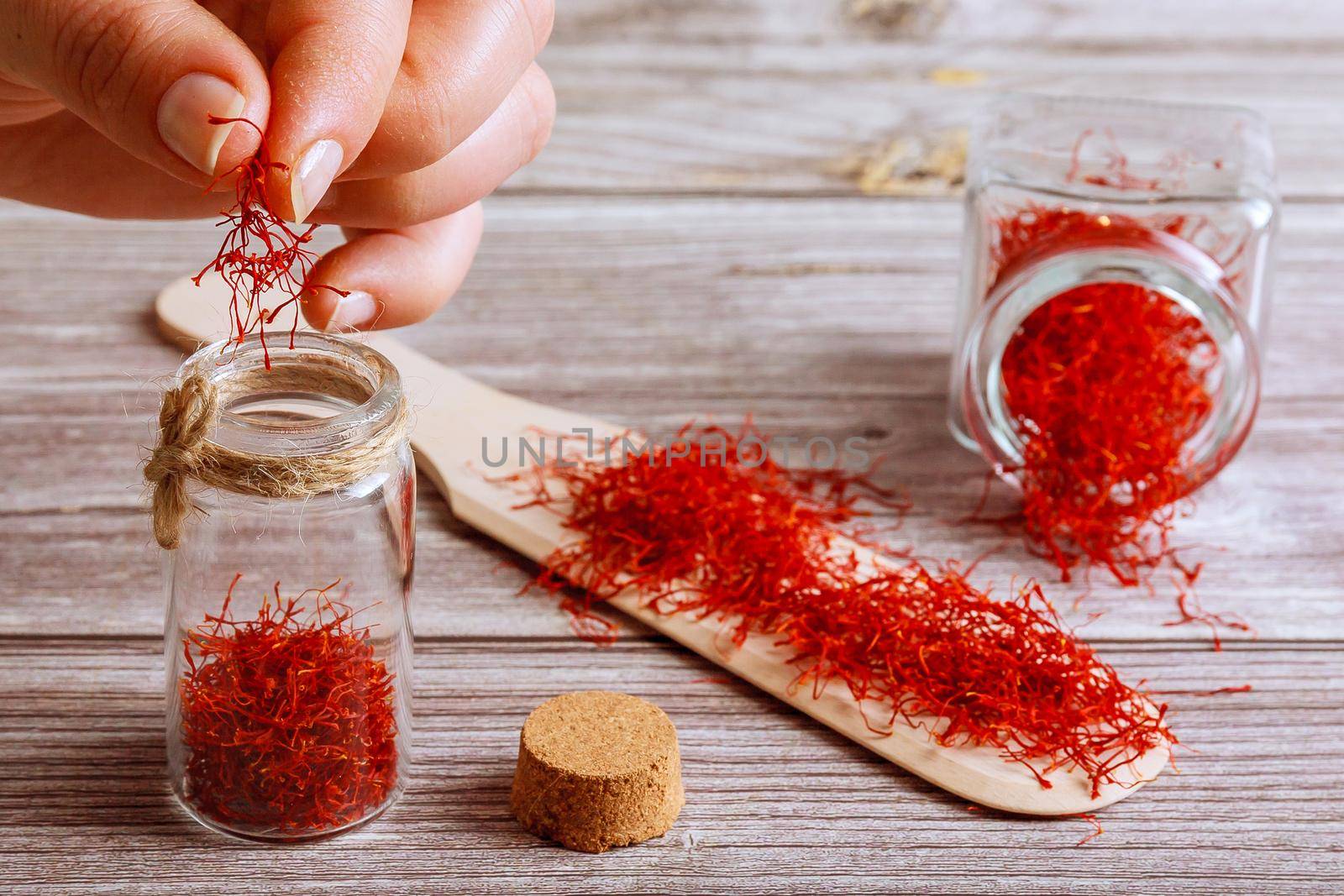The girl puts the saffron in a glass container. Saffron spice in a glass bottle and on a wooden spoon on a wooden background.
