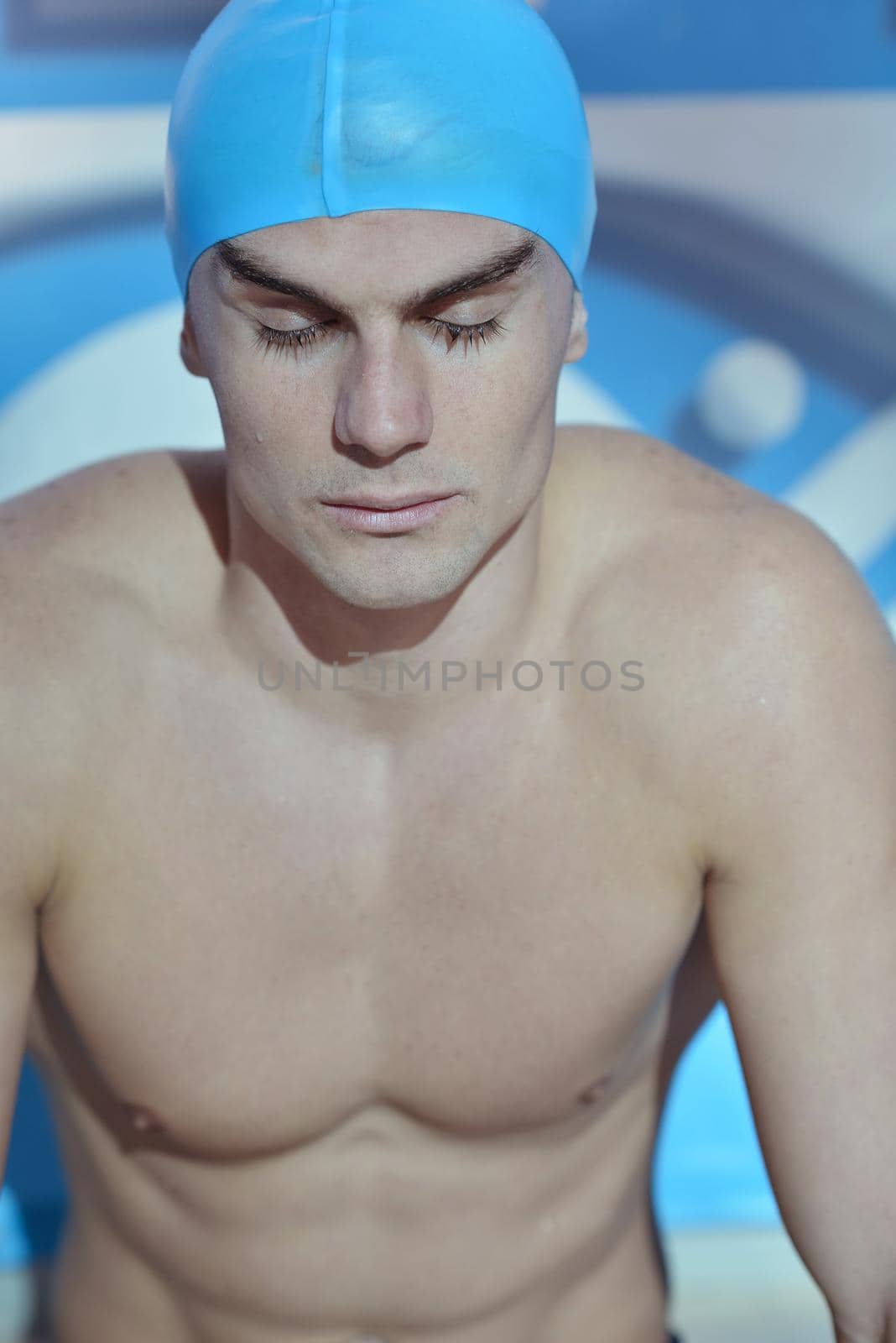 Happy muscular swimmer wearing glasses and cap at swimming pool and represent health and fit concept