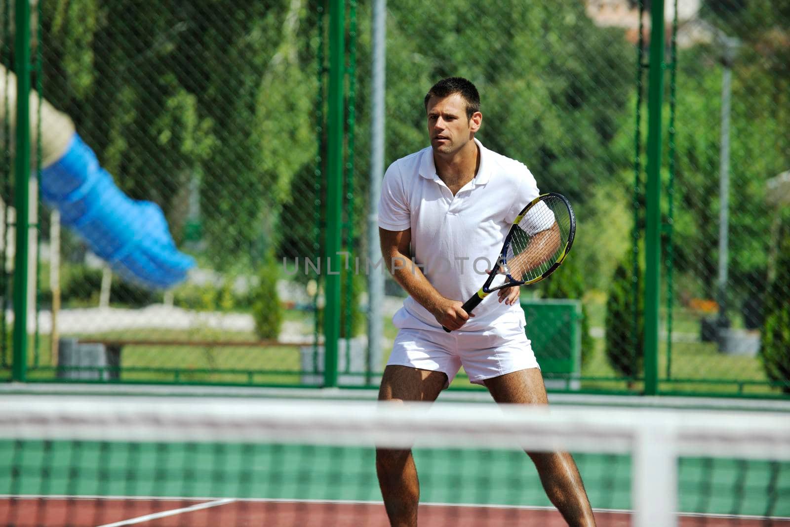 young man play tennis outdoor on orange tennis court at early morning