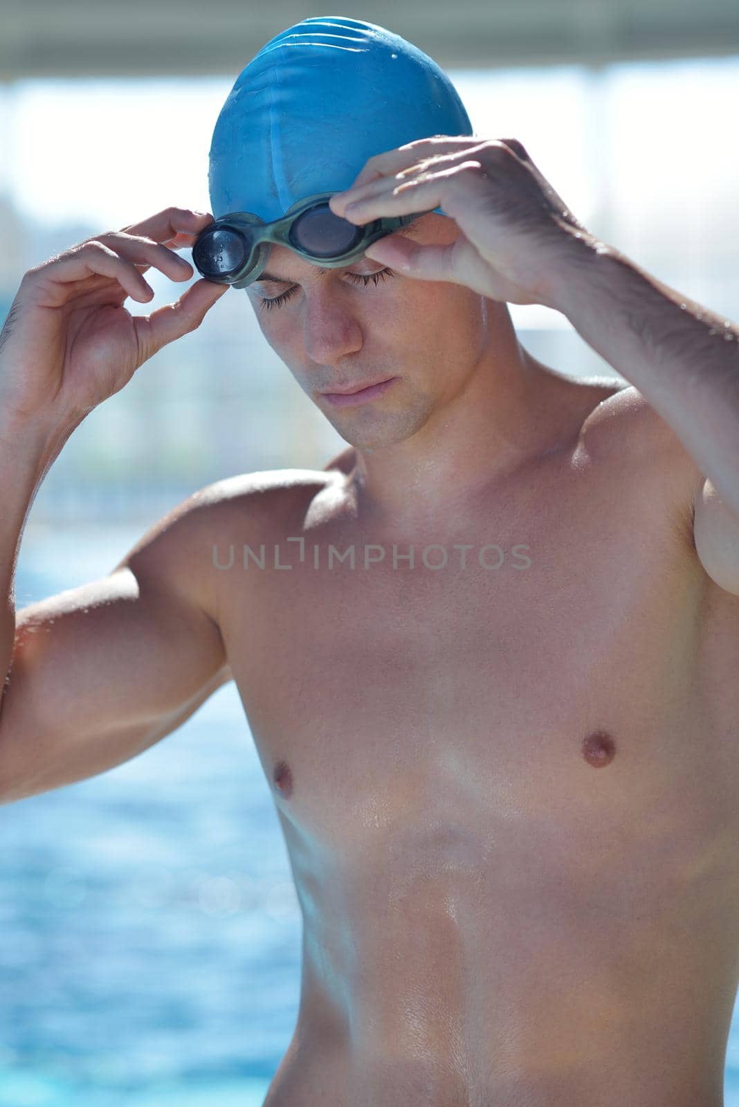 Happy muscular swimmer wearing glasses and cap at swimming pool and represent health and fit concept