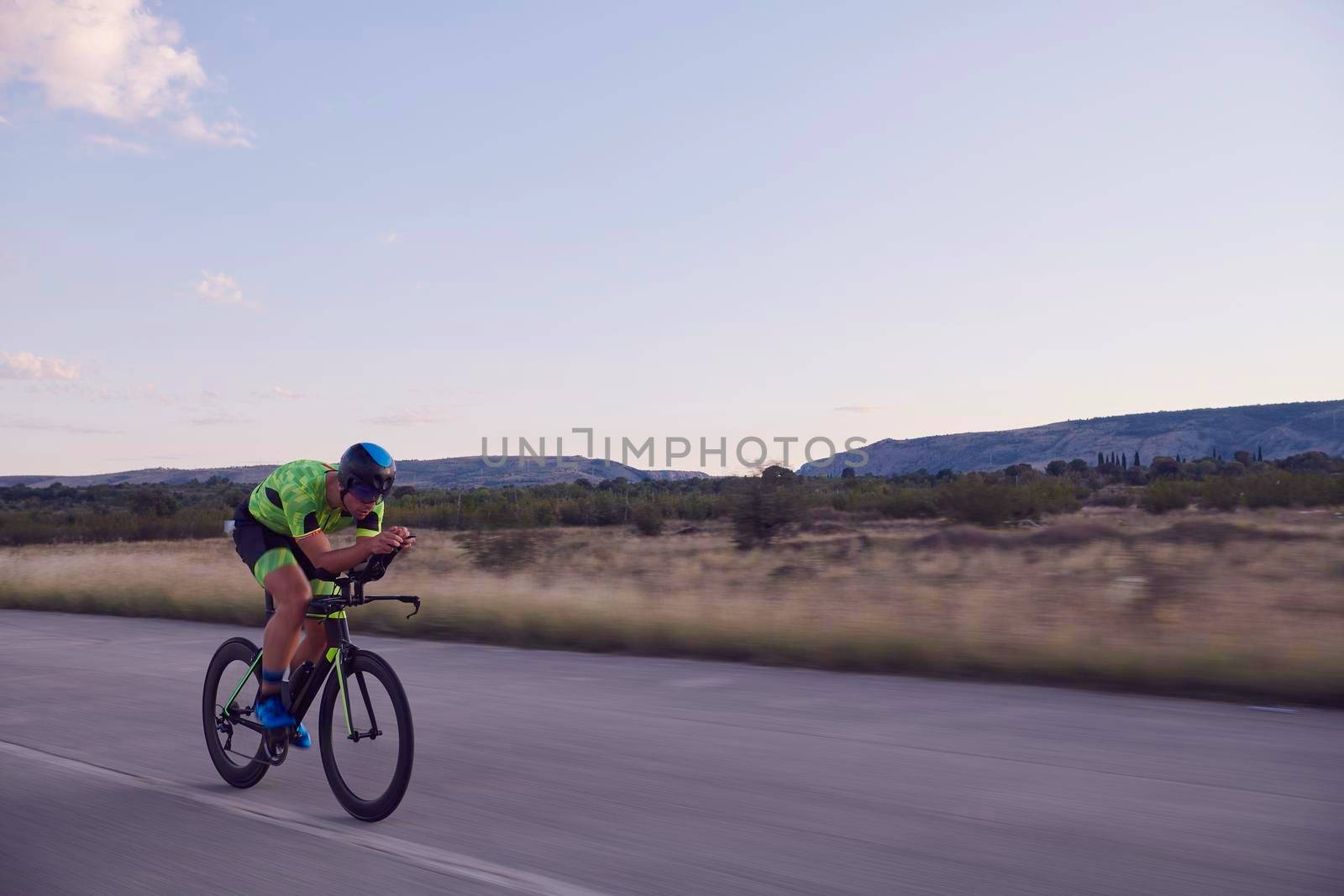 triathlon athlete riding professional racing bike on morning workout sunset or sunrise in background