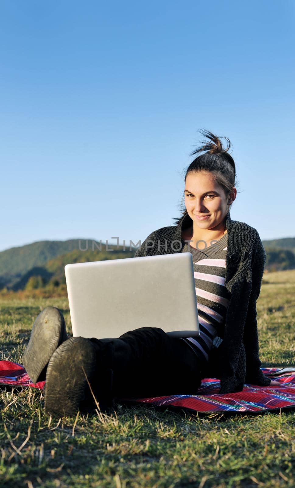 young teen woman work on laptop computer outdoor in nature with blue sky and green grass in background