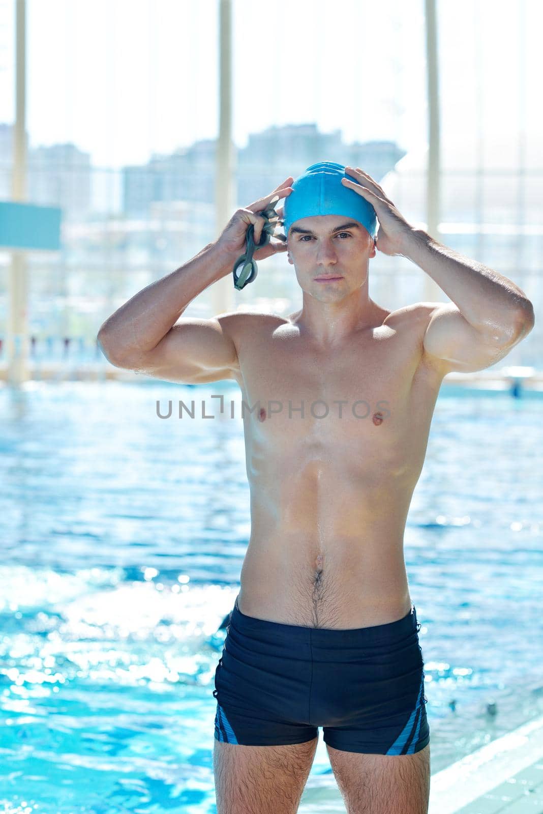 Happy muscular swimmer wearing glasses and cap at swimming pool and represent health and fit concept