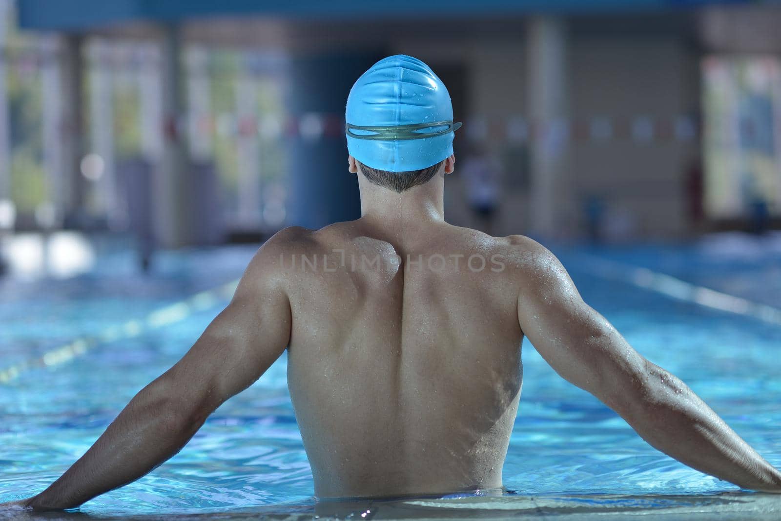 Happy muscular swimmer wearing glasses and cap at swimming pool and represent health and fit concept