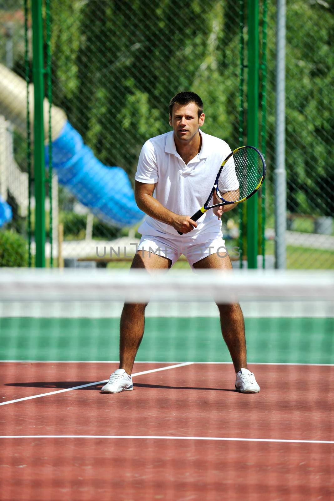 young man play tennis outdoor on orange tennis court at early morning