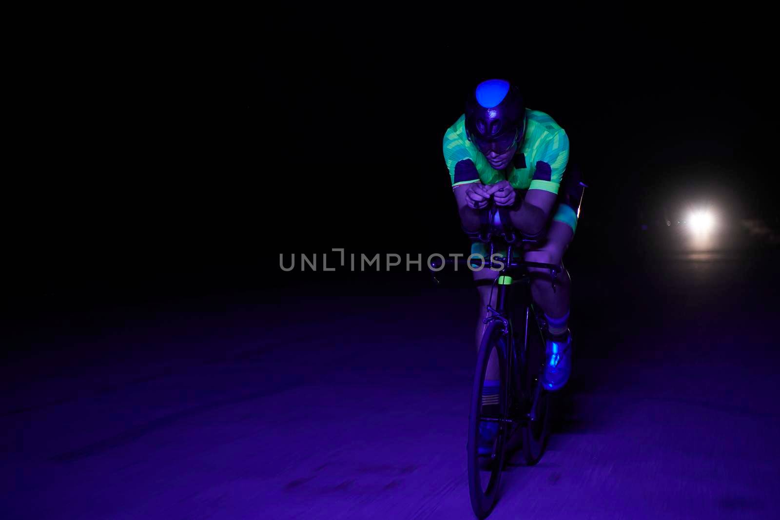 triathlon athlete cycling fast riding professional racing bike at night neon color gel lights