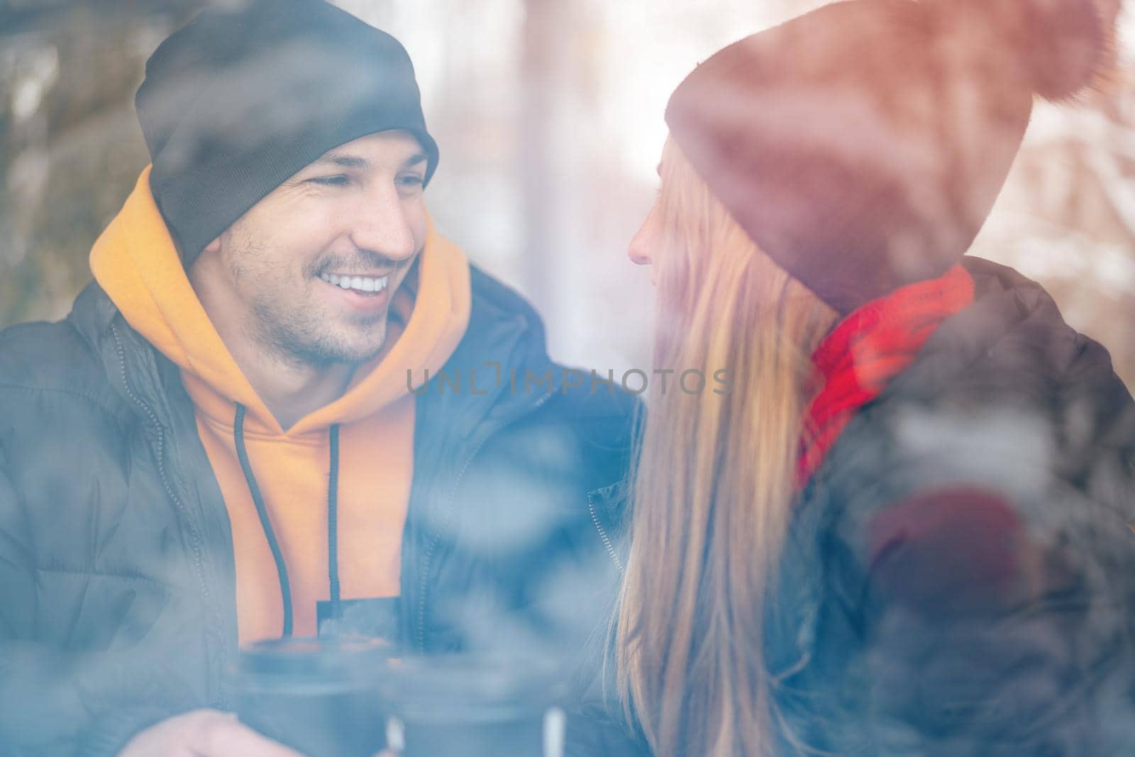 Young loving couple drinking coffee in a cafe behind the glass, view from the street