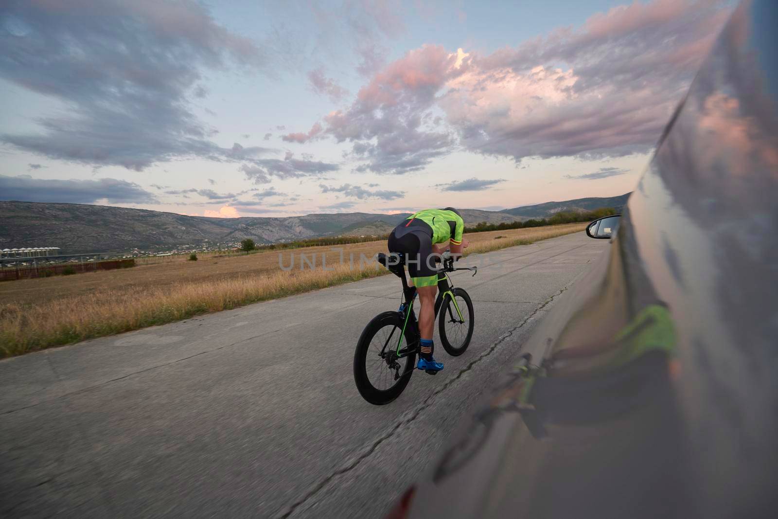 triathlon athlete riding professional racing bike on morning workout sunset or sunrise in background