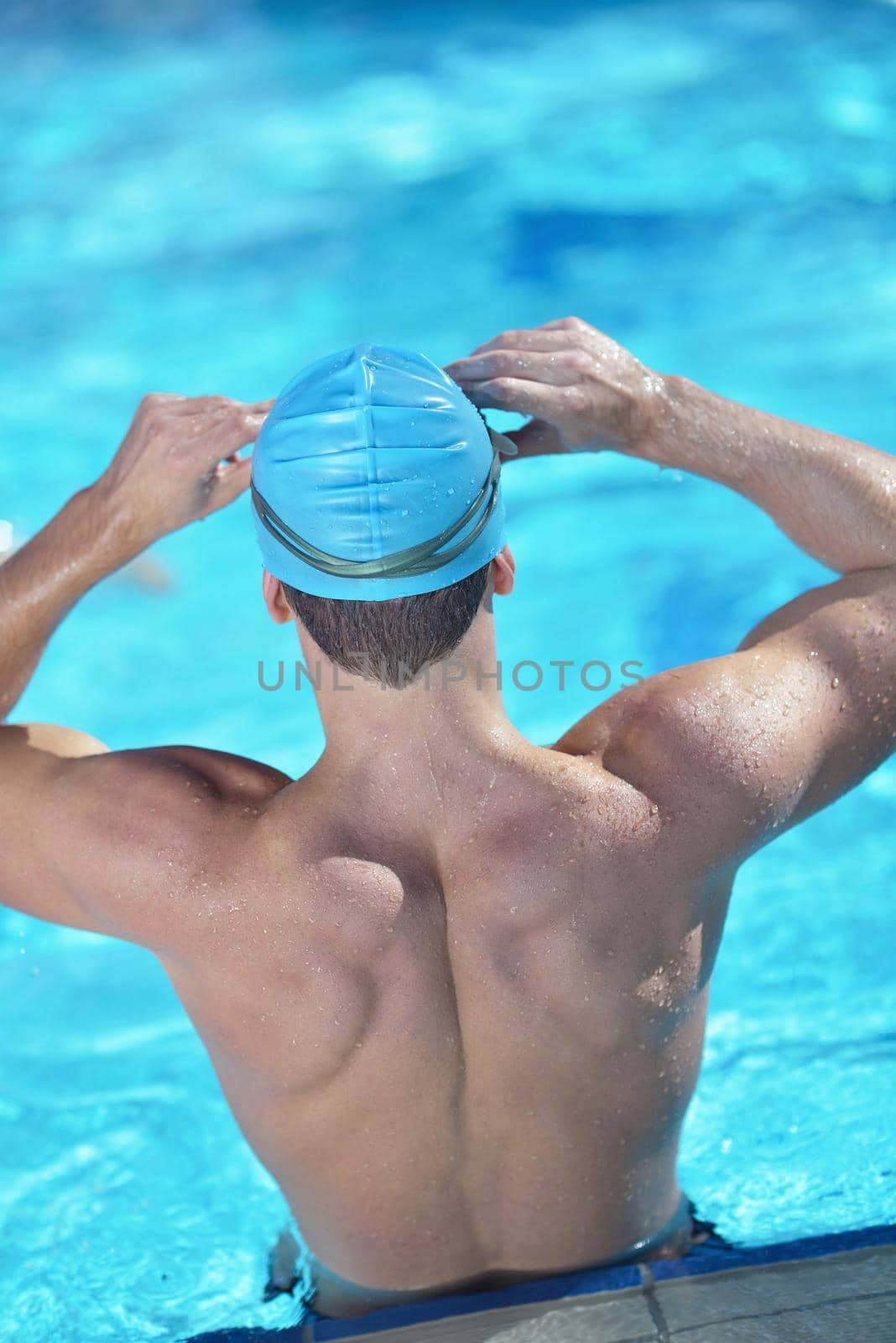 Happy muscular swimmer wearing glasses and cap at swimming pool and represent health and fit concept