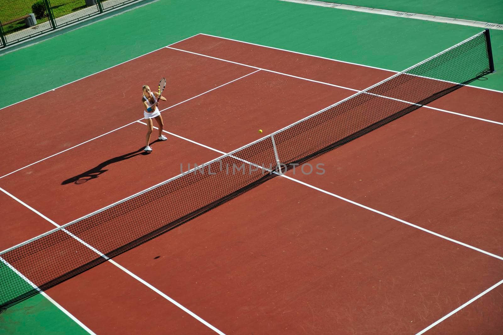 young fit woman play tennis outdoor on orange tennis field at early morning