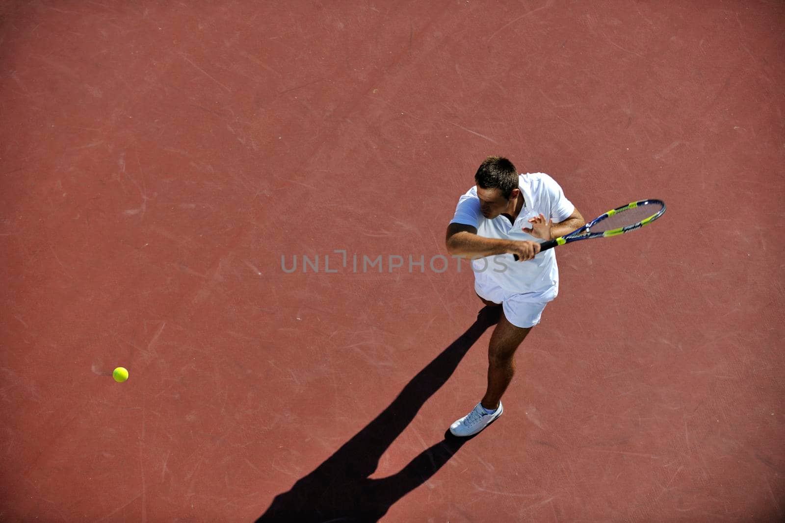 young man play tennis outdoor on orange tennis field at early morning