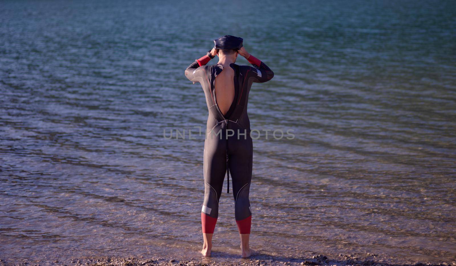 reak triathlon athlete getting ready and prepare goggles hat and  wetsuit for swimming training on lake