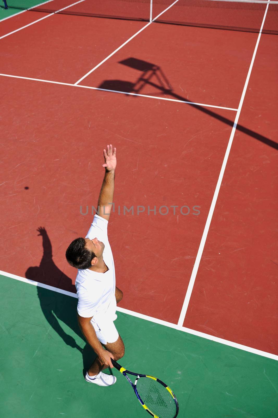 young man play tennis outdoor on orange tennis court at early morning