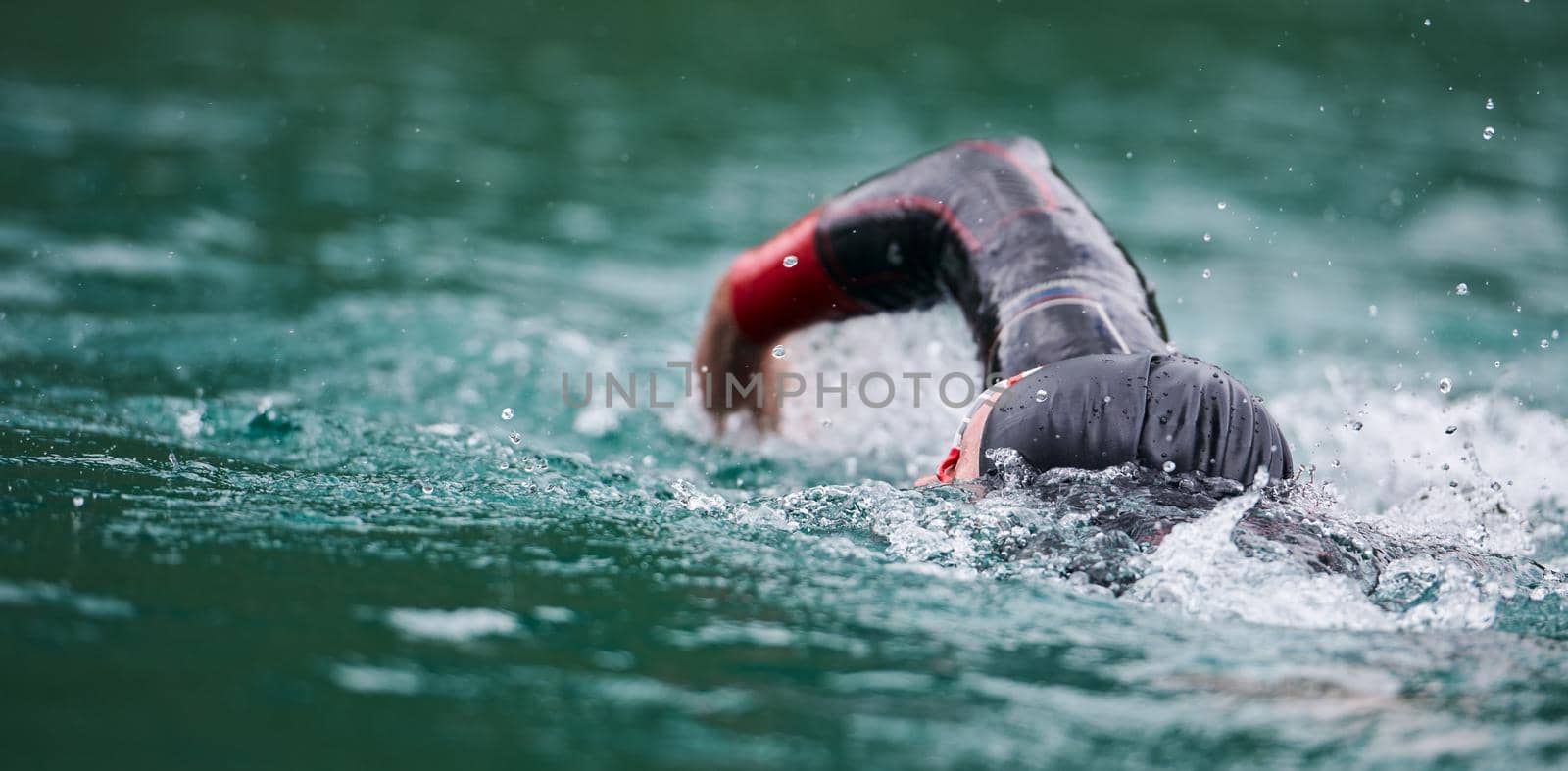 triathlon athlete swimming on lake wearing wetsuit by dotshock