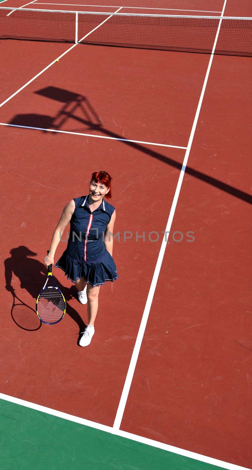 young fit woman play tennis outdoor on orange tennis field at early morning