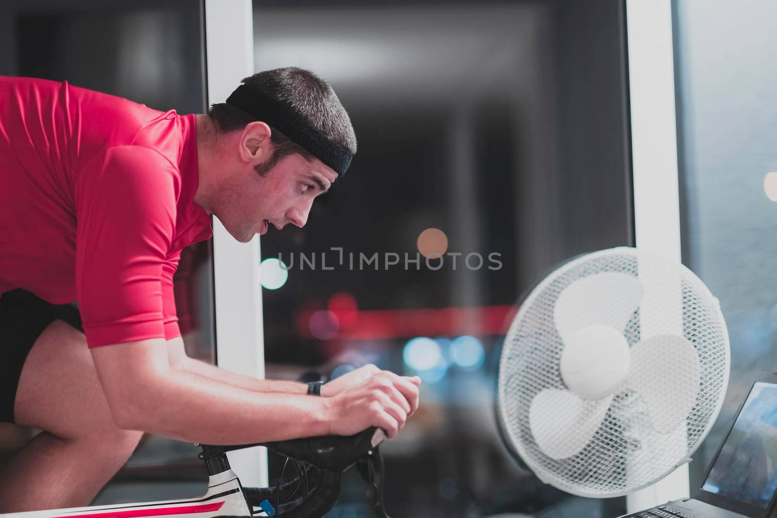 Man cycling on the machine trainer he is exercising in the home at night. Playing online bike racing game during coronavirus covid19 lockdown. New normal concept.