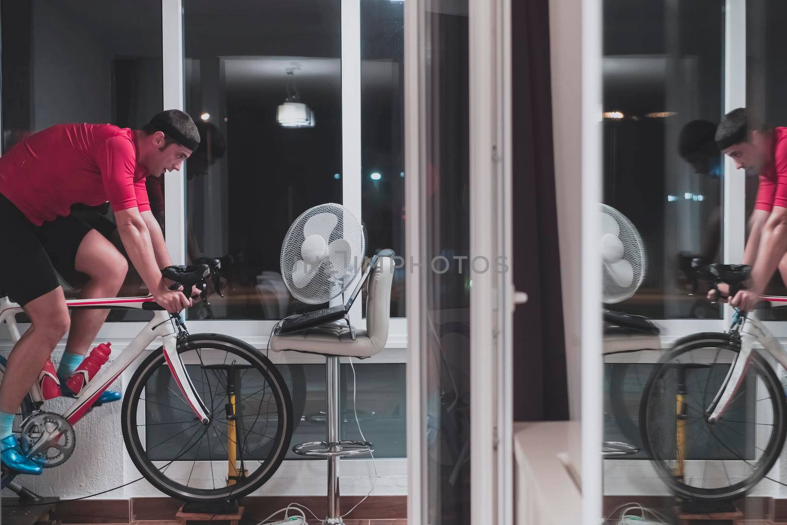 Man cycling on the machine trainer he is exercising in the home at night. Playing online bike racing game during coronavirus covid19 lockdown. New normal concept.