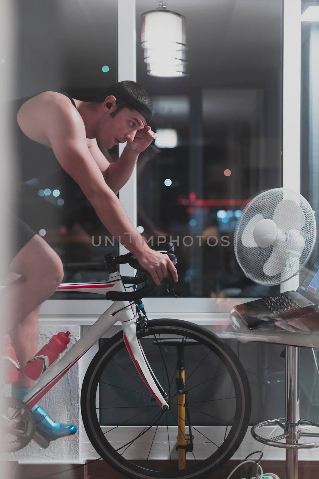 Man cycling on the machine trainer he is exercising in the home at night. Playing online bike racing game during coronavirus covid19 lockdown. New normal concept.