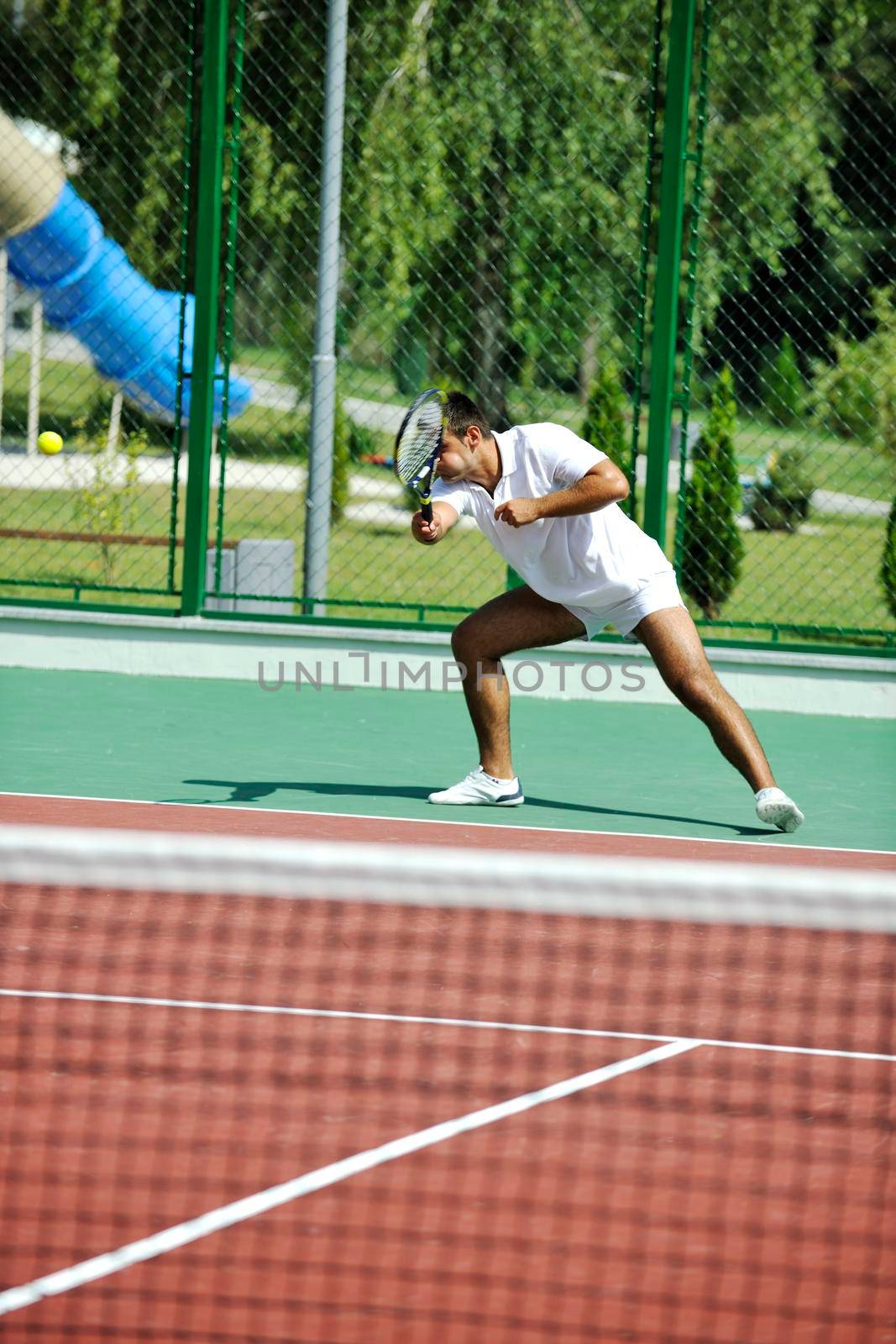 young man play tennis outdoor on orange tennis court at early morning