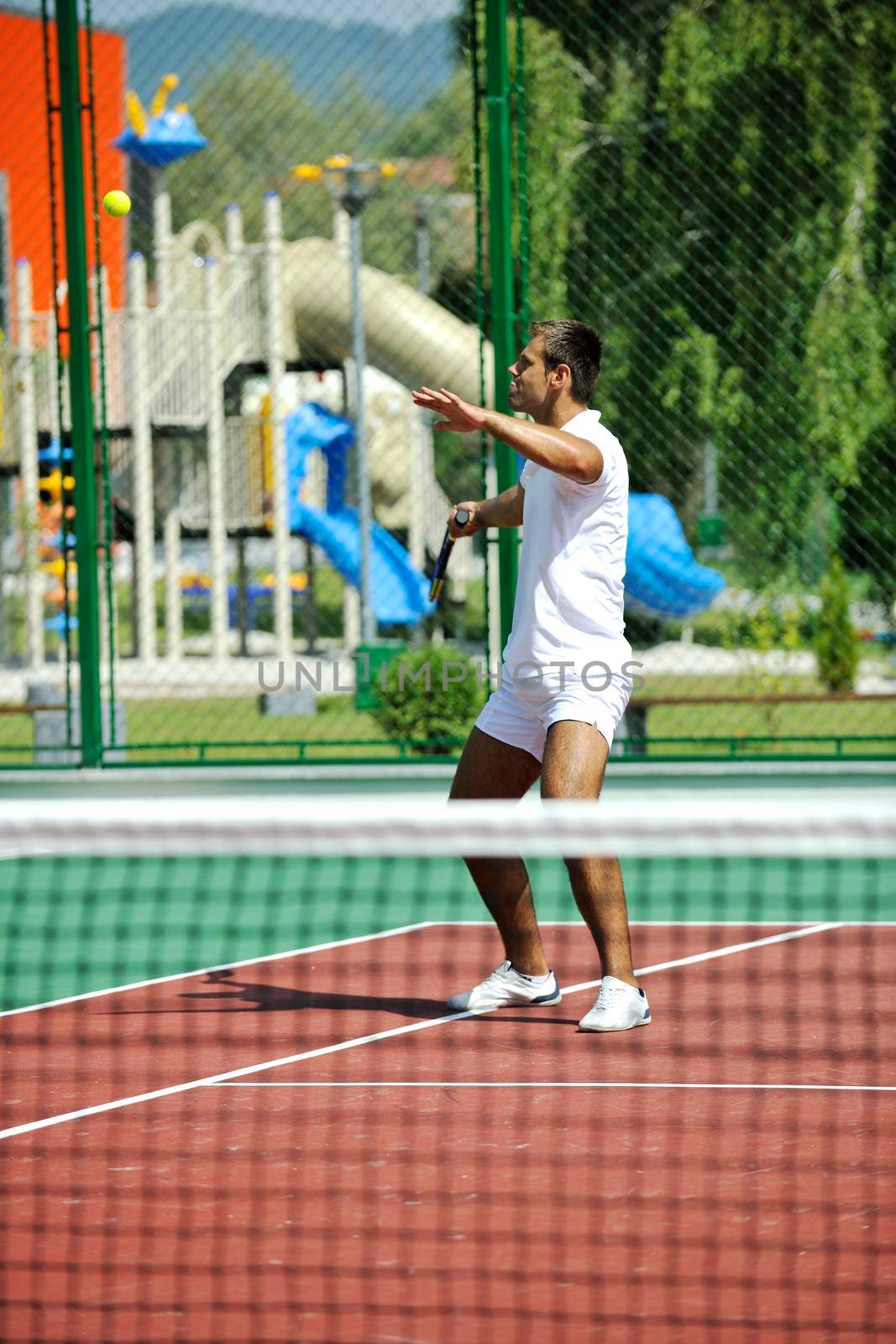 young man play tennis outdoor on orange tennis court at early morning