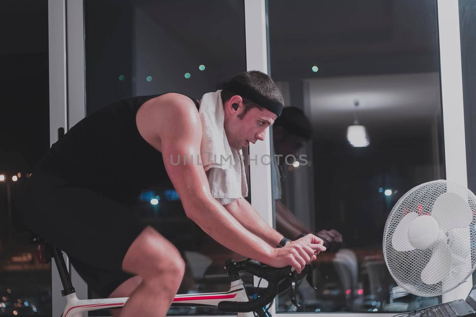 Man cycling on the machine trainer he is exercising in the home at night playing online bike racing game by dotshock