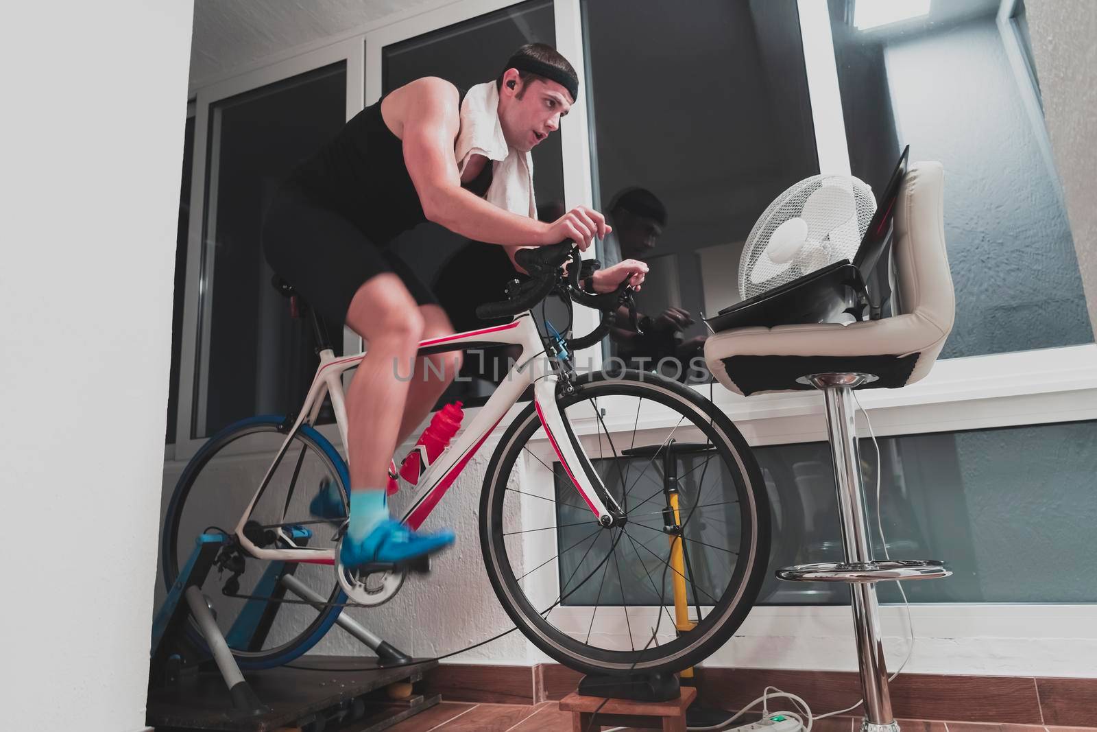 Man cycling on the machine trainer he is exercising in the home at night. Playing online bike racing game during coronavirus covid19 lockdown. New normal concept.