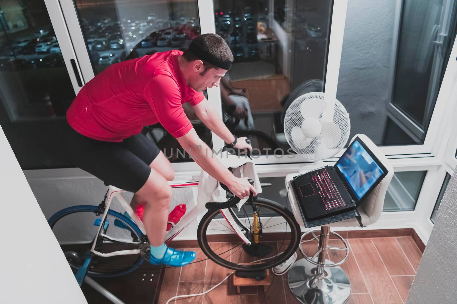 Man cycling on the machine trainer he is exercising in the home at night. Playing online bike racing game during coronavirus covid19 lockdown. New normal concept.