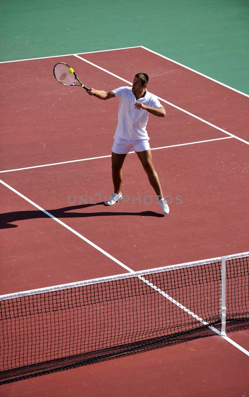 young man play tennis outdoor on orange tennis field at early morning