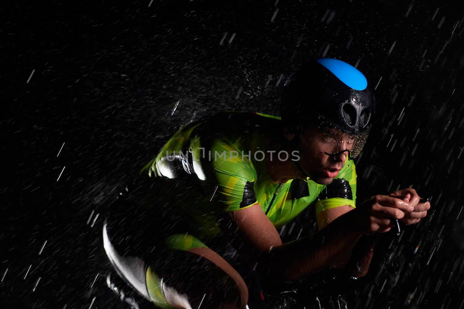 triathlon athlete riding professional racing bike fast  at night with bad weather and falling rain