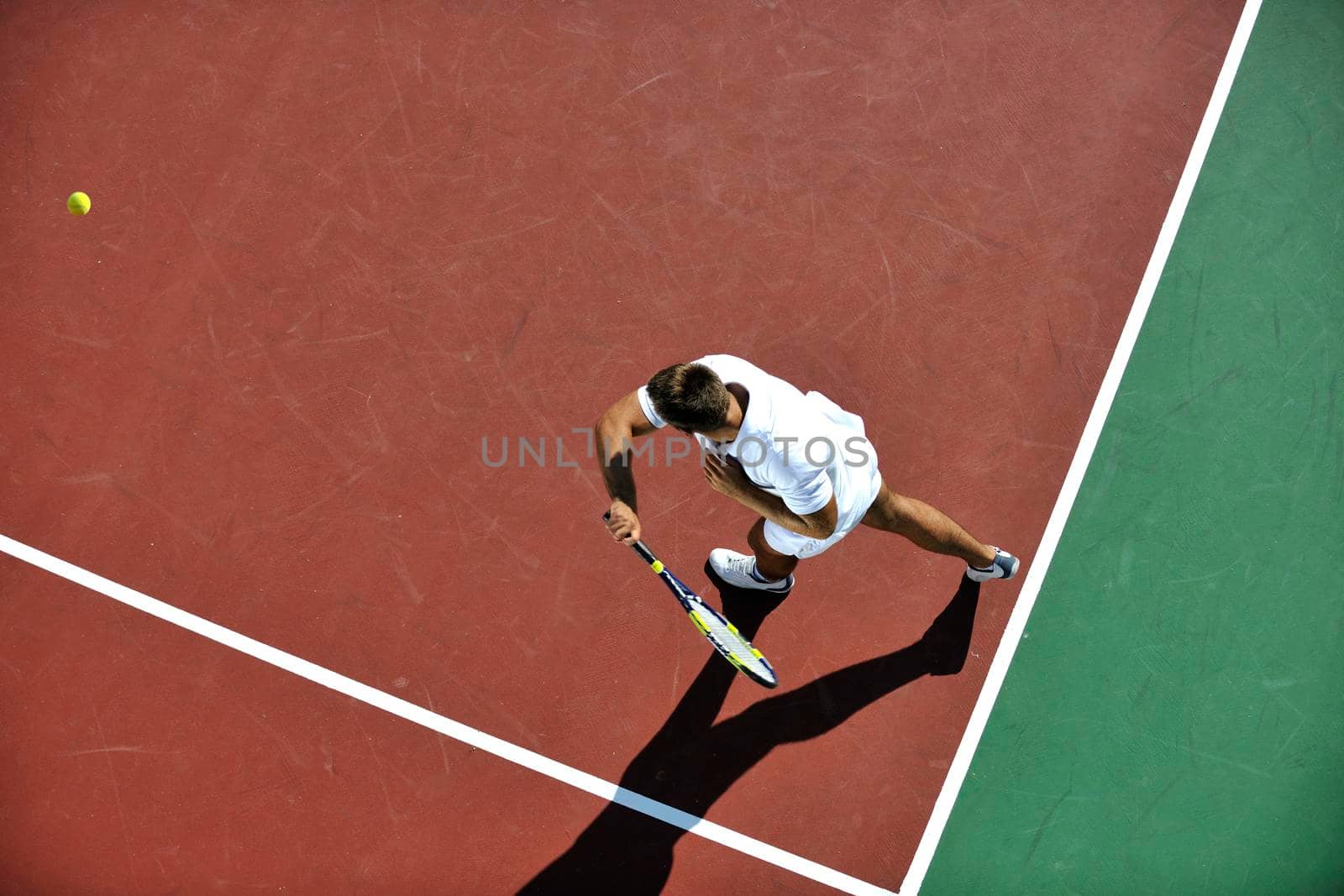 young man play tennis outdoor on orange tennis field at early morning