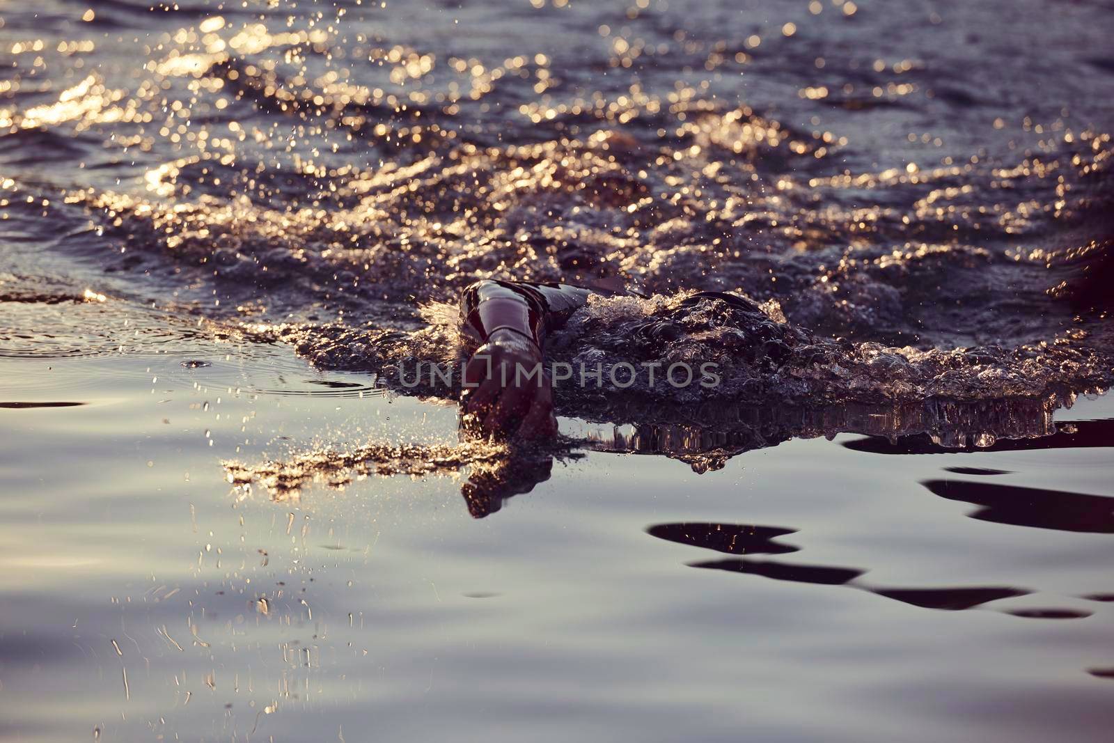 triathlon athlete swimming on lake in sunrise  wearing wetsuit by dotshock