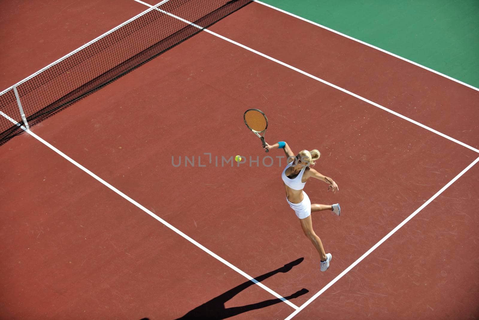 young fit woman play tennis outdoor on orange tennis field at early morning