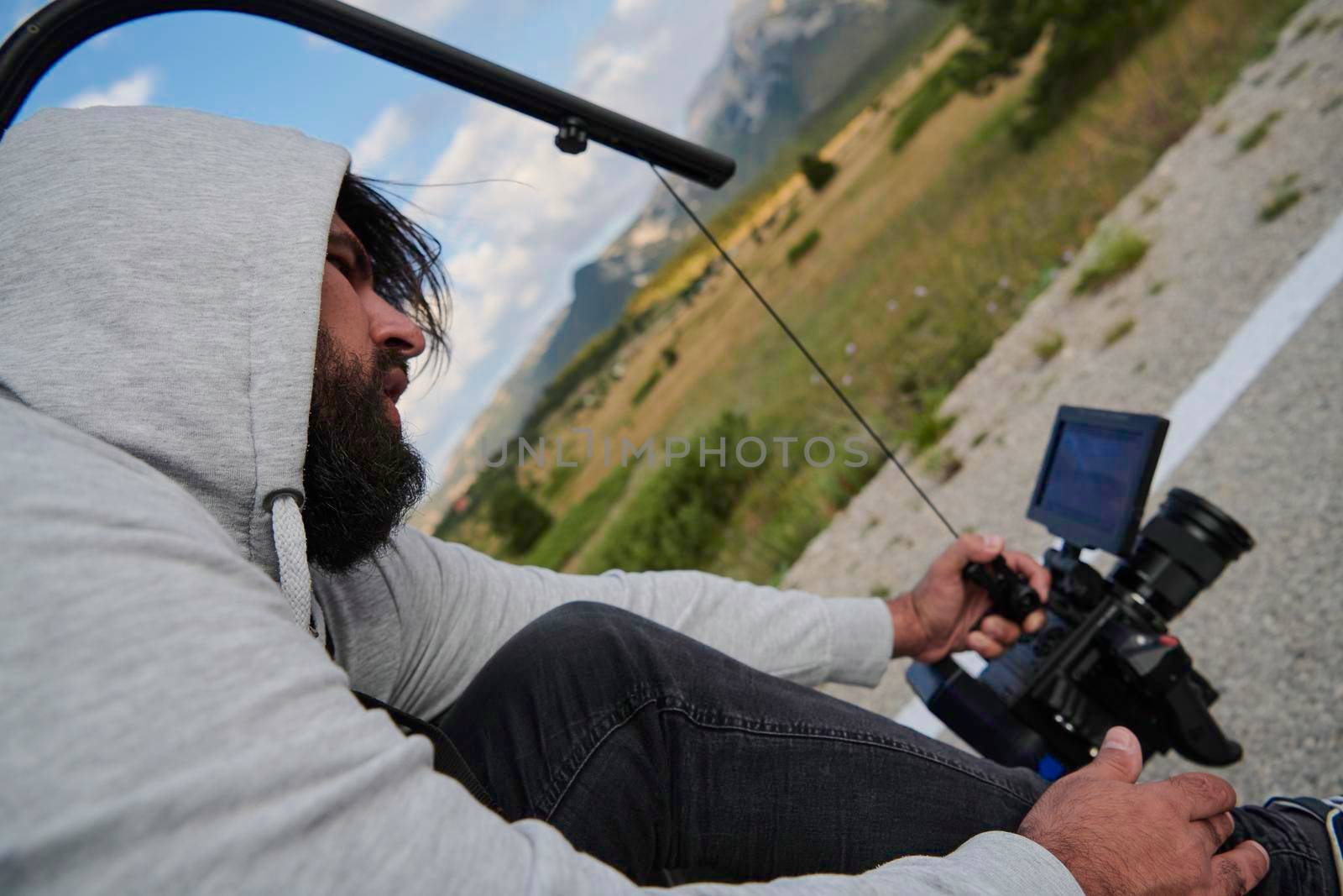 cinematographer with professional cinema camera taking sport action shot  from moving car of triathlon athlete who riding bike on low traffic country road